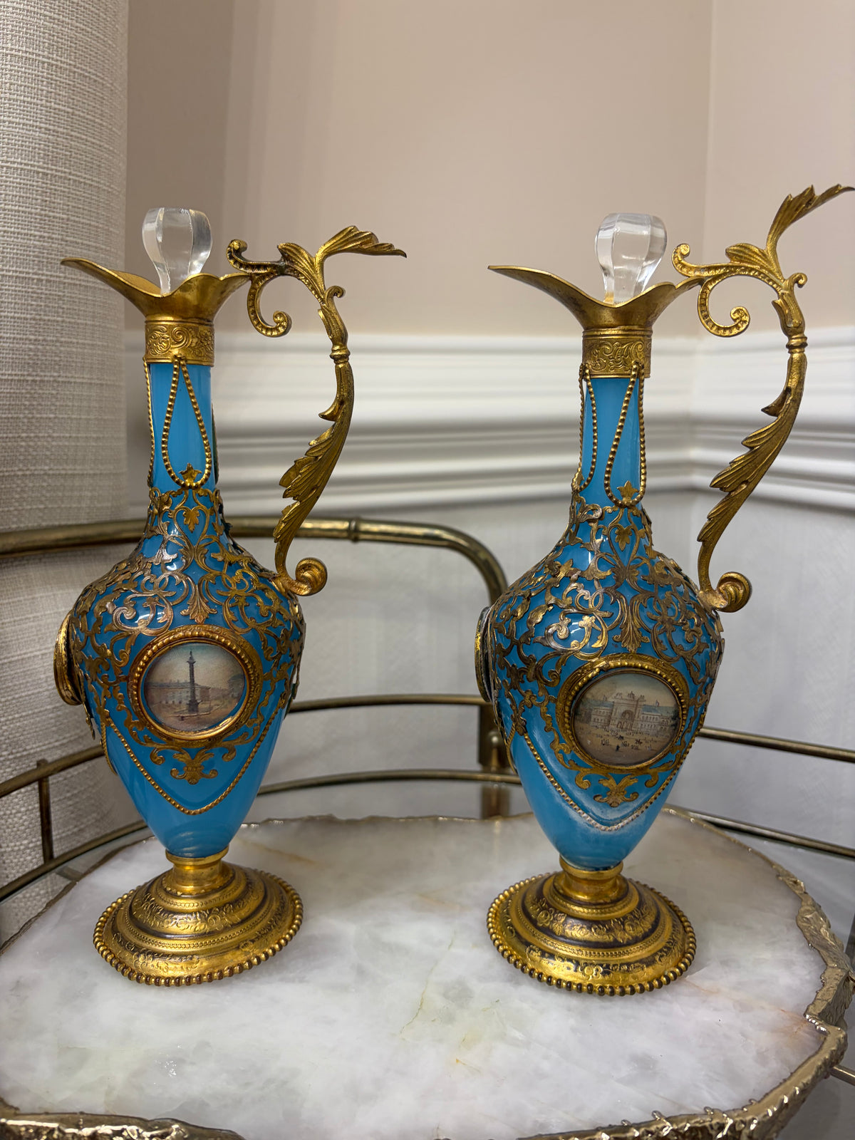 Stunning antique 19th-century French Napoleon III-style blue opaline glass ewer jugs pair adorned with elaborate gilt ormolu (gold-plated bronze) mounts, scrollwork, and scenic medallions! Circa 1836-1850