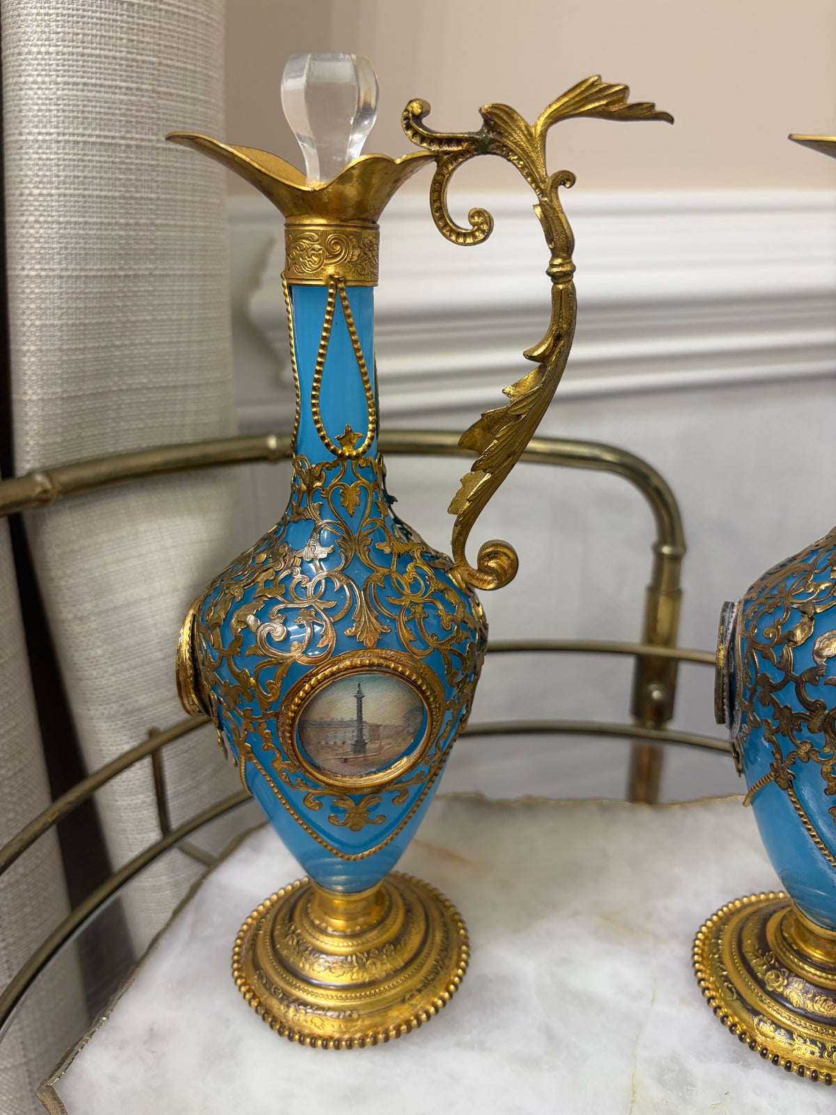 Stunning antique 19th-century French Napoleon III-style blue opaline glass ewer jugs pair adorned with elaborate gilt ormolu (gold-plated bronze) mounts, scrollwork, and scenic medallions! Circa 1836-1850