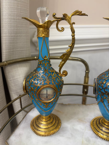 Stunning antique 19th-century French Napoleon III-style blue opaline glass ewer jugs pair adorned with elaborate gilt ormolu (gold-plated bronze) mounts, scrollwork, and scenic medallions! Circa 1836-1850