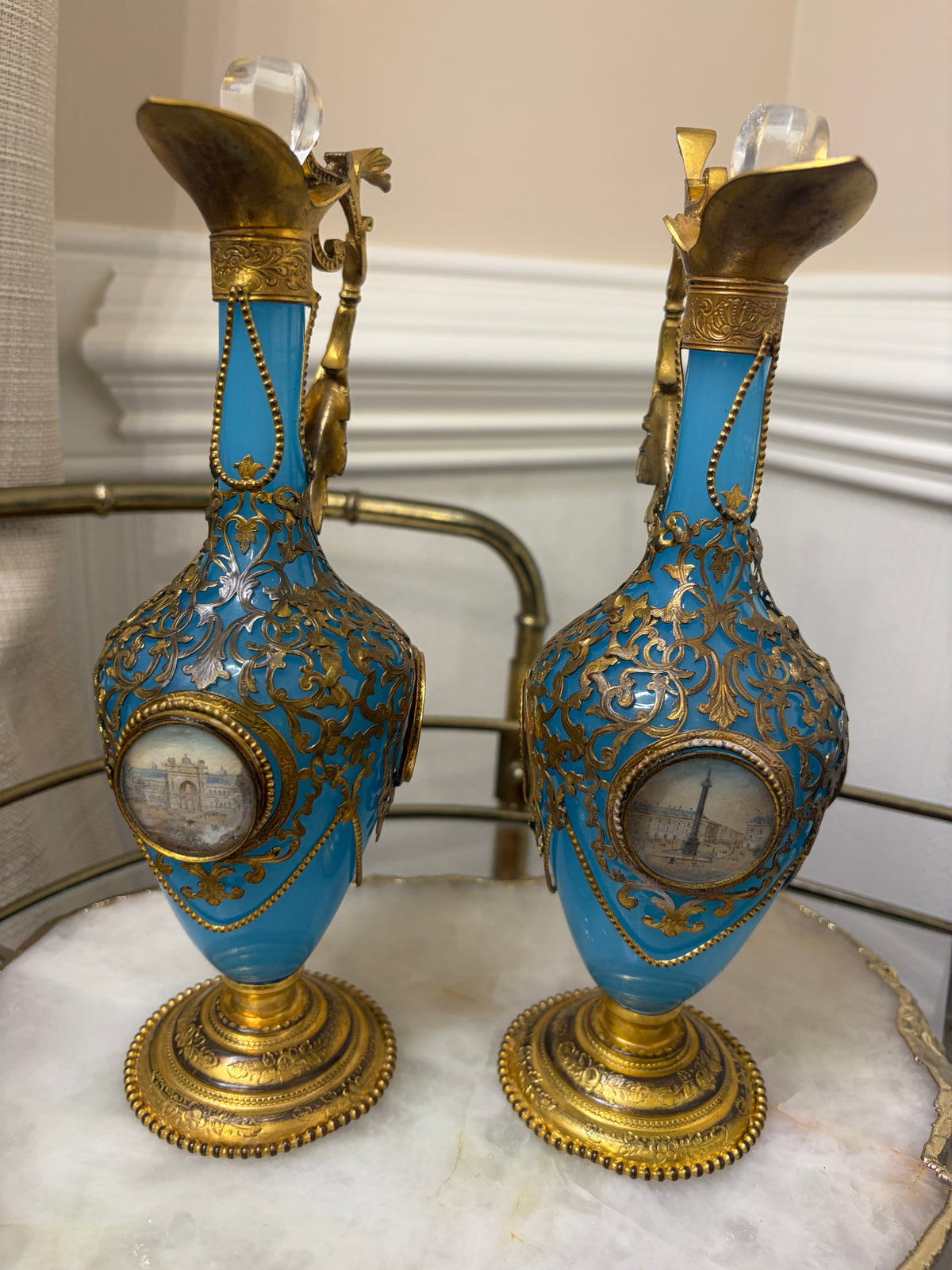 Stunning antique 19th-century French Napoleon III-style blue opaline glass ewer jugs pair adorned with elaborate gilt ormolu (gold-plated bronze) mounts, scrollwork, and scenic medallions! Circa 1836-1850