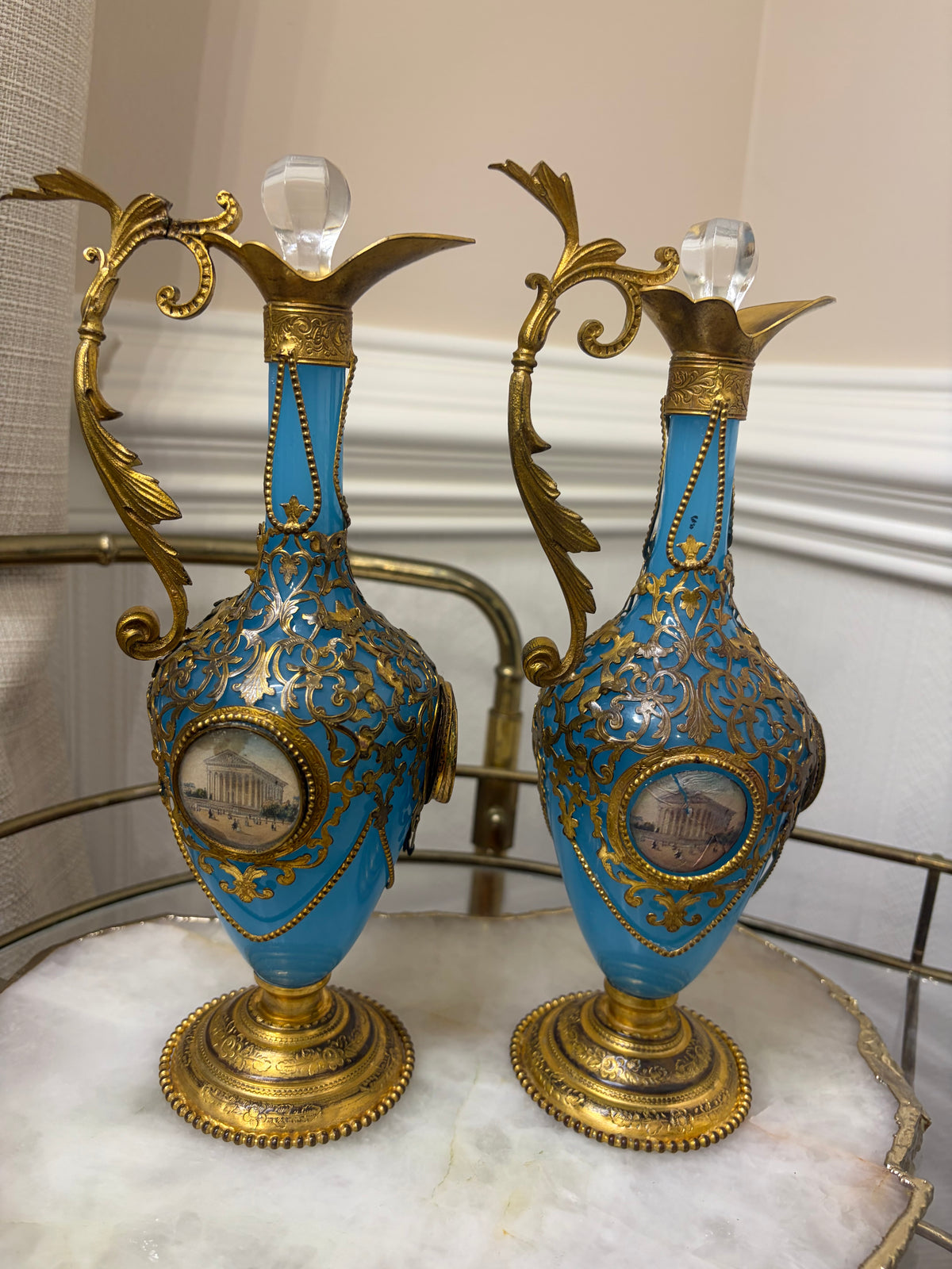 Stunning antique 19th-century French Napoleon III-style blue opaline glass ewer jugs pair adorned with elaborate gilt ormolu (gold-plated bronze) mounts, scrollwork, and scenic medallions! Circa 1836-1850